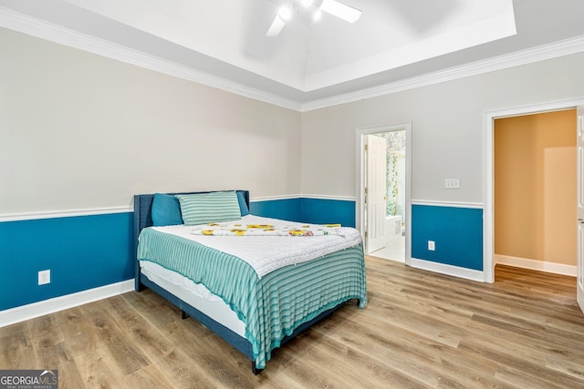 bedroom featuring ceiling fan, connected bathroom, wood-type flooring, ornamental molding, and a raised ceiling