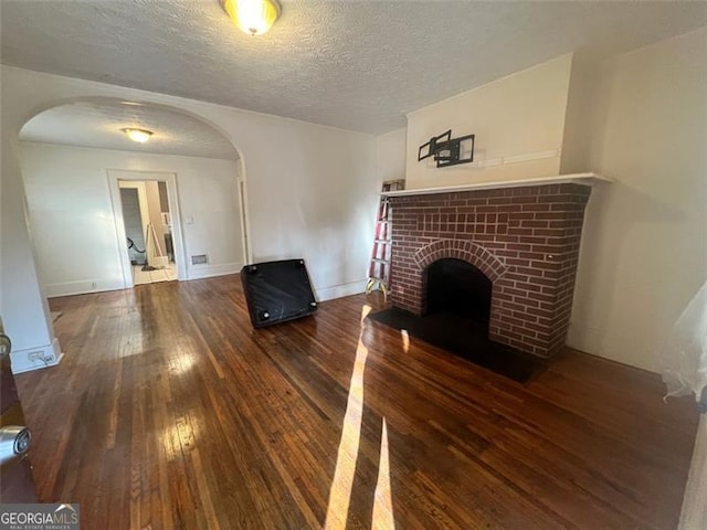 unfurnished living room with a textured ceiling, a brick fireplace, and dark wood-type flooring