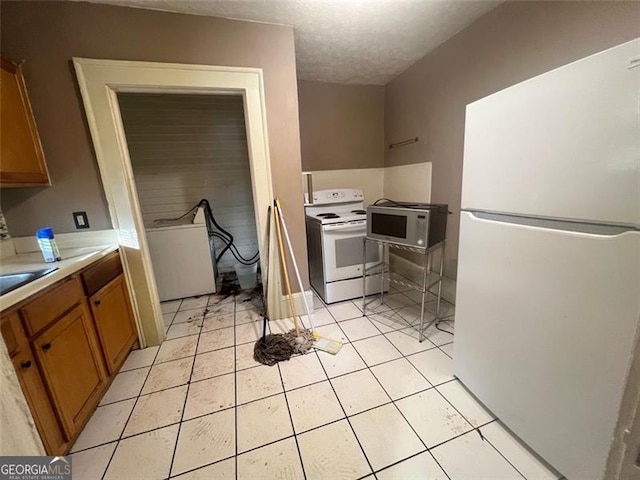 kitchen with sink, white appliances, a textured ceiling, and light tile patterned floors