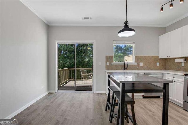 kitchen featuring hanging light fixtures, light hardwood / wood-style flooring, white cabinets, and stainless steel dishwasher