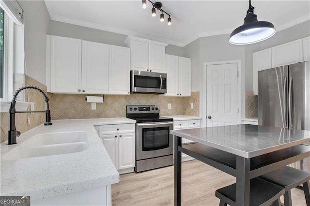 kitchen with ornamental molding, stainless steel appliances, sink, pendant lighting, and white cabinetry