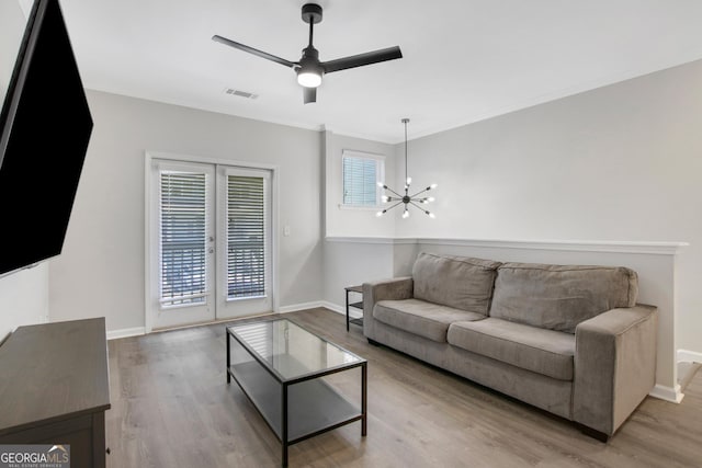 living room featuring wood finished floors, visible vents, crown molding, baseboards, and ceiling fan with notable chandelier