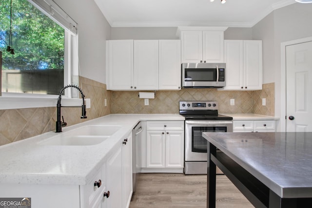 kitchen with white cabinetry, a sink, stainless steel appliances, ornamental molding, and light wood finished floors