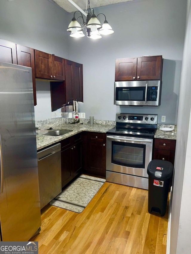 kitchen featuring light stone countertops, stainless steel appliances, pendant lighting, an inviting chandelier, and light hardwood / wood-style floors