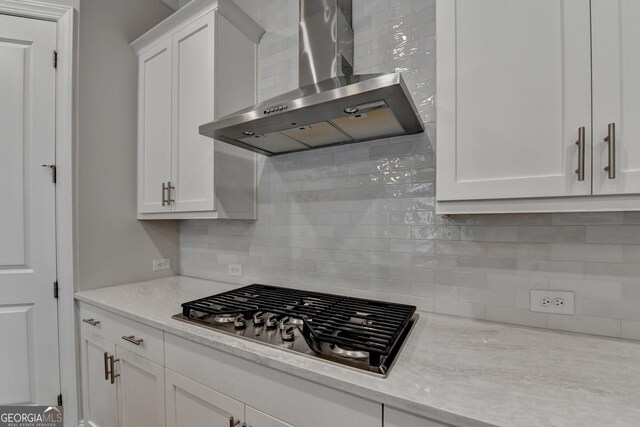 kitchen with light stone countertops, tasteful backsplash, wall chimney range hood, white cabinetry, and stainless steel gas stovetop