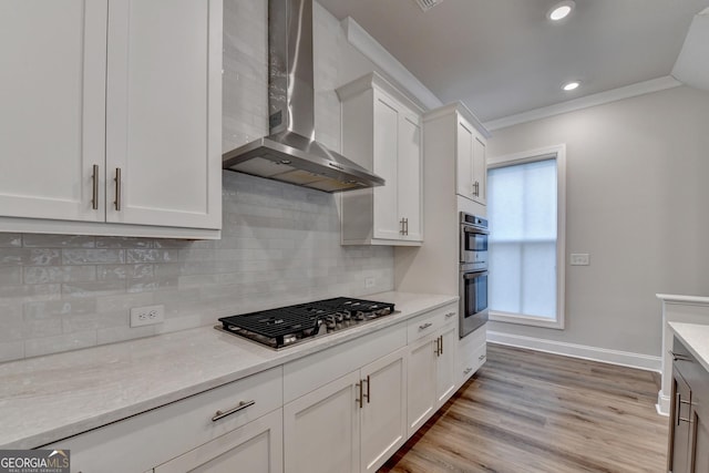 kitchen featuring light wood-type flooring, stainless steel appliances, crown molding, wall chimney range hood, and white cabinetry