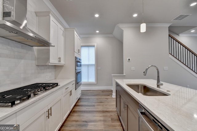 kitchen with crown molding, sink, wall chimney exhaust hood, appliances with stainless steel finishes, and white cabinetry