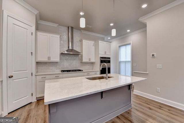 kitchen featuring black gas stovetop, wall chimney exhaust hood, sink, pendant lighting, and white cabinets