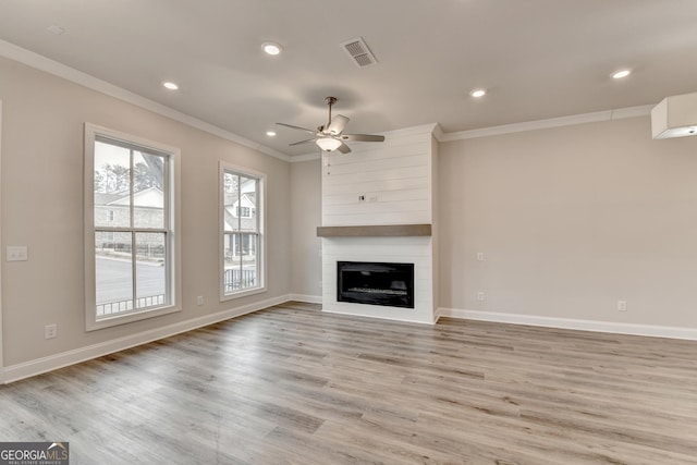 unfurnished living room with ceiling fan, a large fireplace, crown molding, and light wood-type flooring