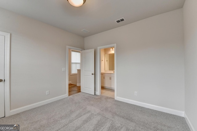 unfurnished bedroom featuring connected bathroom and light colored carpet