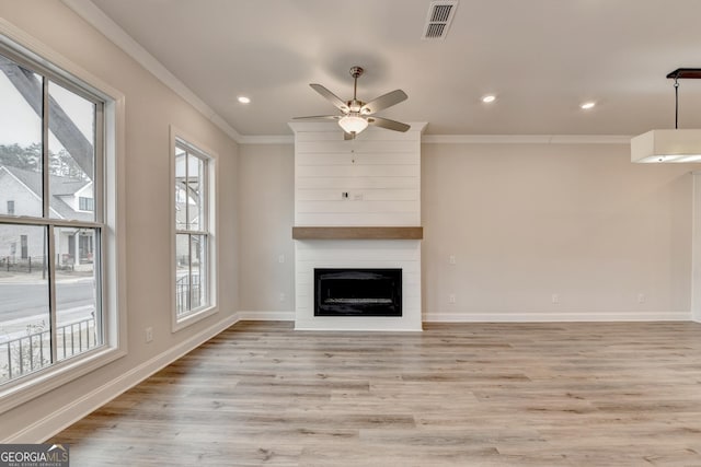 unfurnished living room with ceiling fan, a large fireplace, ornamental molding, and light wood-type flooring