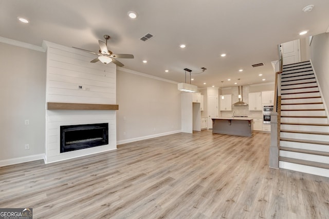 unfurnished living room featuring ceiling fan, light wood-type flooring, ornamental molding, and a fireplace