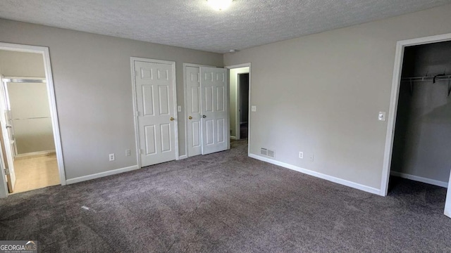 unfurnished bedroom featuring dark colored carpet, a textured ceiling, and two closets