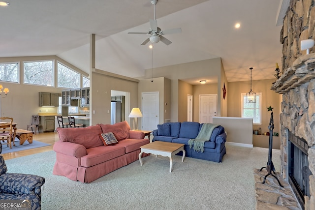 living room with ceiling fan with notable chandelier, a stone fireplace, light colored carpet, and high vaulted ceiling