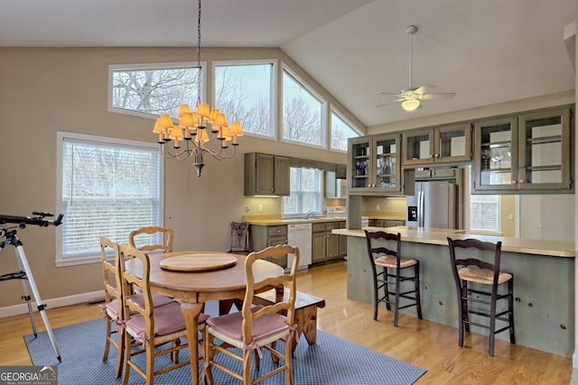 dining room with ceiling fan with notable chandelier, light hardwood / wood-style floors, and high vaulted ceiling