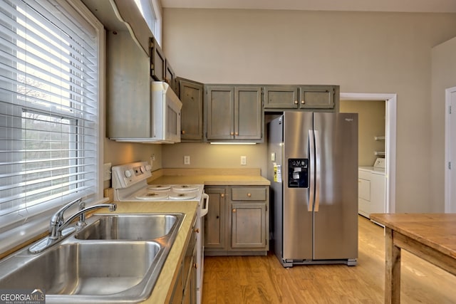 kitchen with washing machine and dryer, sink, stainless steel appliances, and light hardwood / wood-style flooring