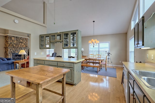 kitchen with sink, an inviting chandelier, a stone fireplace, pendant lighting, and light wood-type flooring