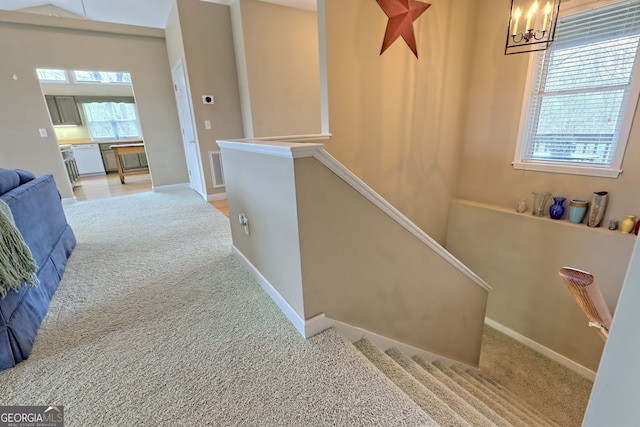 stairs with carpet flooring, a healthy amount of sunlight, and a notable chandelier