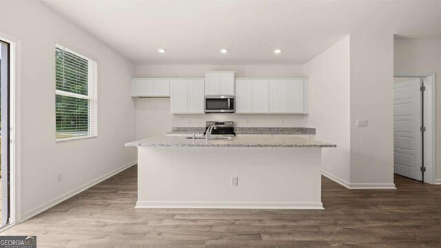 kitchen with hardwood / wood-style flooring, a center island with sink, light stone countertops, and appliances with stainless steel finishes