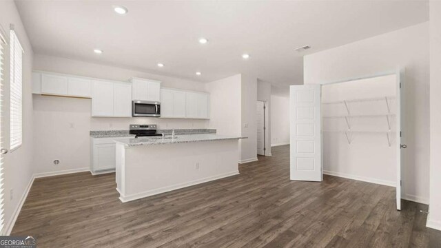 kitchen with light stone countertops, dark hardwood / wood-style floors, an island with sink, white cabinets, and appliances with stainless steel finishes