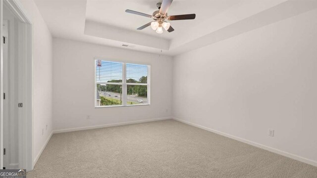 unfurnished room featuring ceiling fan, carpet floors, and a tray ceiling