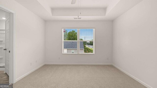 empty room with a raised ceiling, ceiling fan, and carpet floors