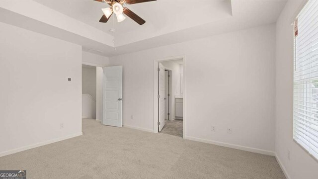 unfurnished bedroom with ceiling fan, ensuite bathroom, light carpet, and a tray ceiling