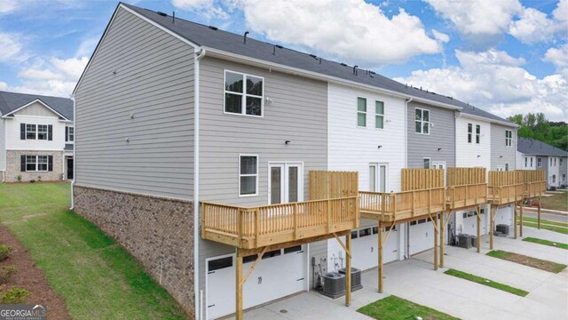 rear view of house featuring a lawn, a wooden deck, central AC unit, and a garage