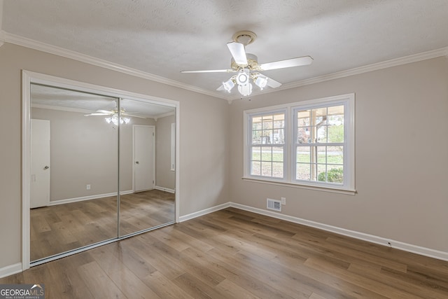 unfurnished bedroom with a closet, ceiling fan, crown molding, a textured ceiling, and light hardwood / wood-style flooring