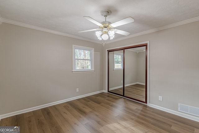 unfurnished bedroom featuring hardwood / wood-style flooring, ceiling fan, crown molding, and a closet