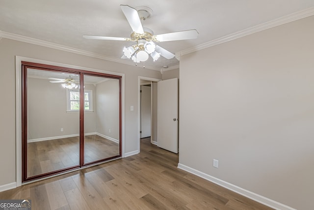 unfurnished bedroom featuring crown molding, light hardwood / wood-style floors, ceiling fan, and a closet