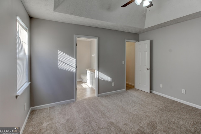 unfurnished bedroom featuring ceiling fan, a textured ceiling, connected bathroom, and light carpet