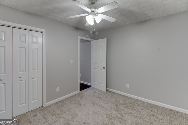 unfurnished bedroom featuring ceiling fan, a closet, light carpet, and a textured ceiling