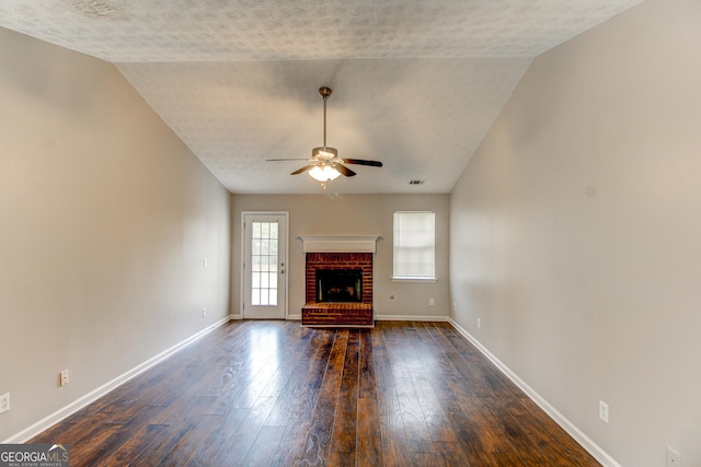 unfurnished living room with ceiling fan, a brick fireplace, dark hardwood / wood-style flooring, a textured ceiling, and vaulted ceiling