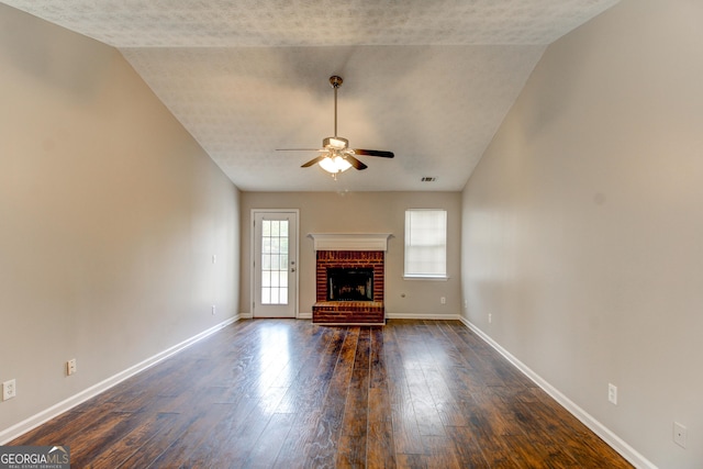 unfurnished living room with ceiling fan, vaulted ceiling, dark hardwood / wood-style floors, and a brick fireplace