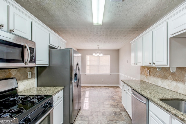 kitchen featuring stainless steel appliances, an inviting chandelier, light stone counters, pendant lighting, and white cabinets