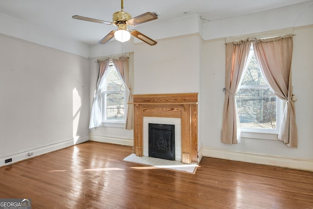 unfurnished living room with wood-type flooring, ceiling fan, and a tiled fireplace