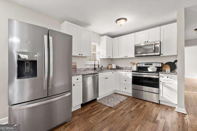 kitchen with sink, light stone countertops, dark hardwood / wood-style flooring, white cabinetry, and stainless steel appliances