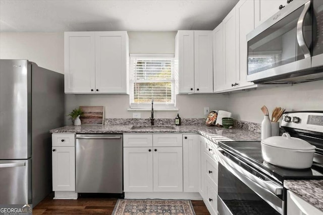 kitchen with light stone counters, stainless steel appliances, dark wood-type flooring, sink, and white cabinets