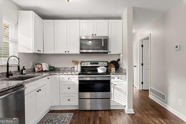 kitchen with white cabinets, appliances with stainless steel finishes, light stone counters, and sink