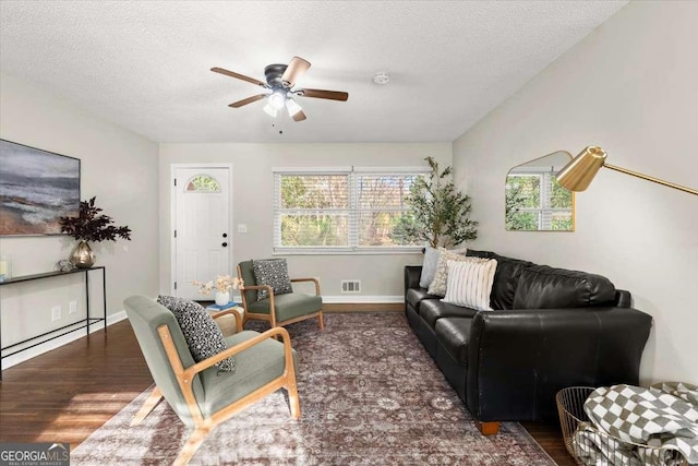 living room with a textured ceiling, ceiling fan, and dark hardwood / wood-style floors