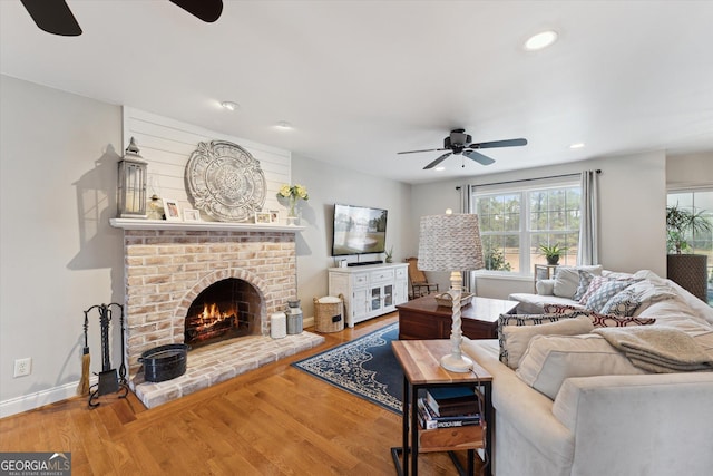 living room featuring ceiling fan, wood-type flooring, and a brick fireplace