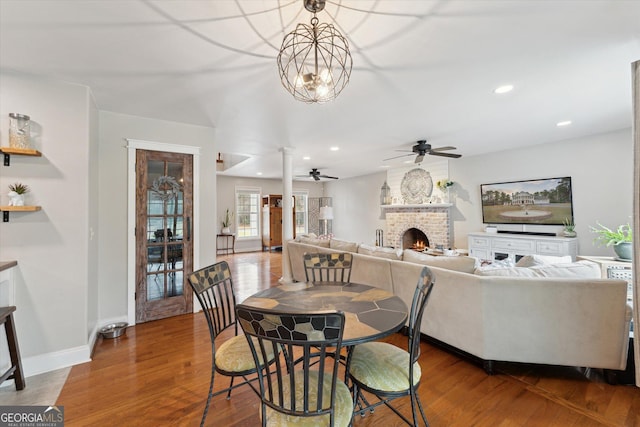 dining area featuring a brick fireplace, ceiling fan with notable chandelier, and hardwood / wood-style flooring