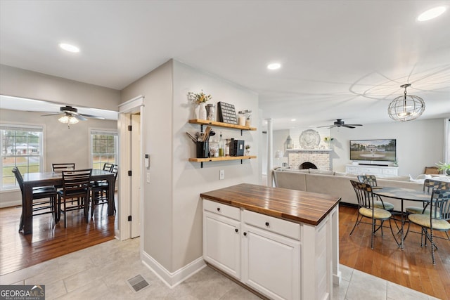 kitchen with wood counters, a fireplace, ceiling fan, white cabinets, and light hardwood / wood-style floors