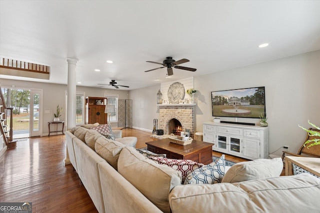 living room featuring hardwood / wood-style floors, ornate columns, ceiling fan, and a brick fireplace