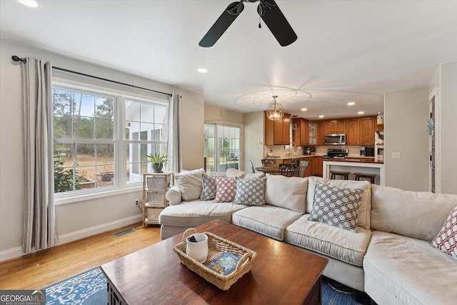 living room featuring ceiling fan with notable chandelier and light wood-type flooring