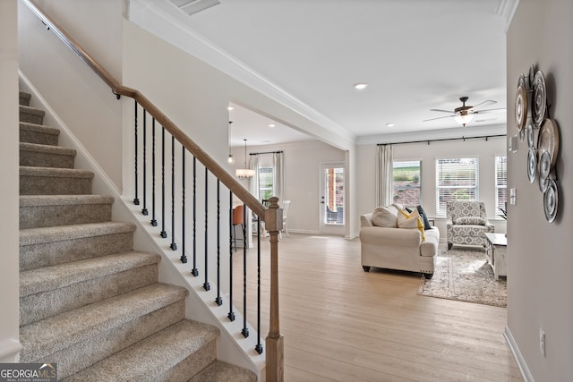 living room with ceiling fan with notable chandelier, light hardwood / wood-style floors, a healthy amount of sunlight, and crown molding