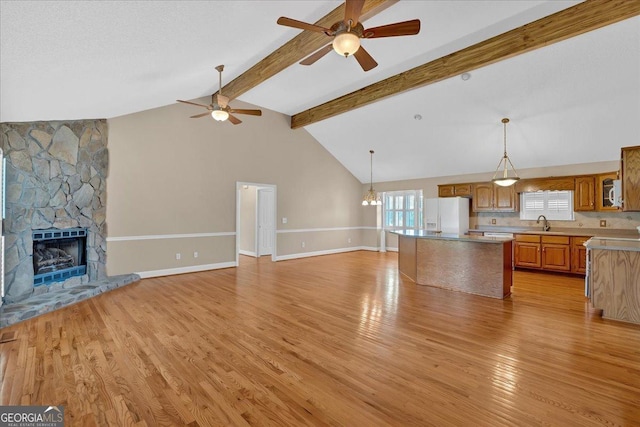 unfurnished living room featuring a fireplace, beam ceiling, light wood-type flooring, and ceiling fan