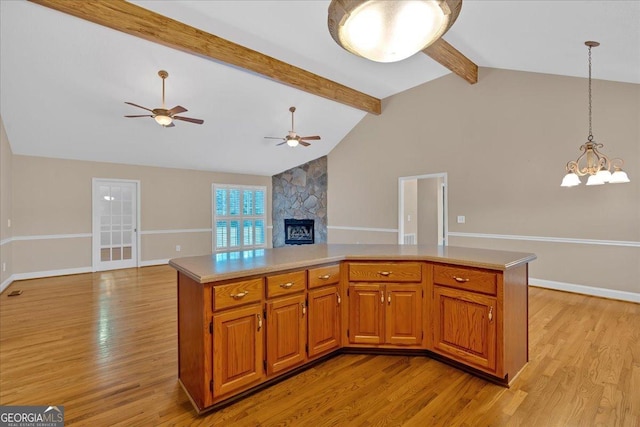 kitchen featuring beamed ceiling, pendant lighting, a fireplace, and light hardwood / wood-style flooring