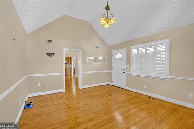 entryway with high vaulted ceiling, light hardwood / wood-style floors, a textured ceiling, and a notable chandelier